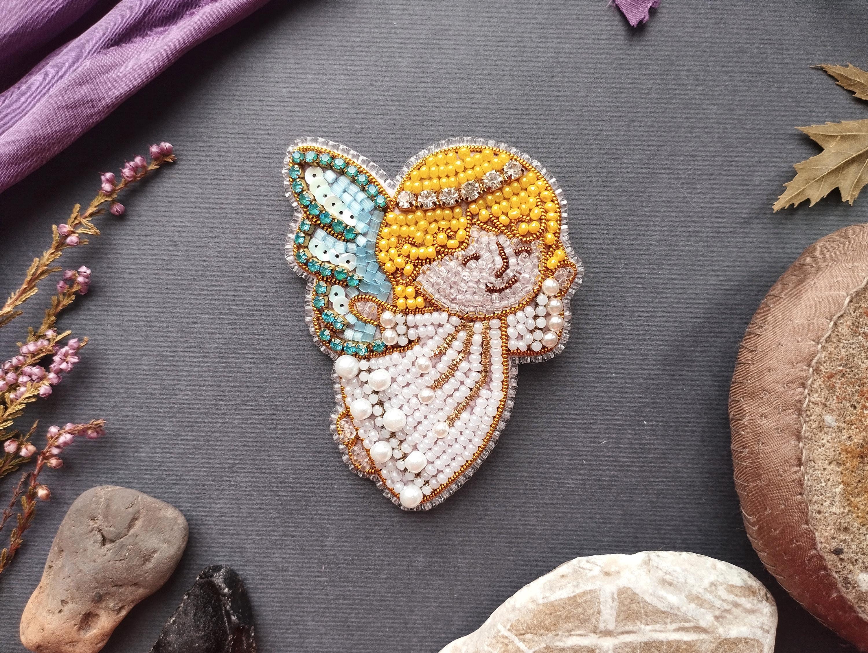 a decorative piece of embroidered art, including a butterfly motif, surrounded by various natural elements such as flowers, rocks, and leaves.